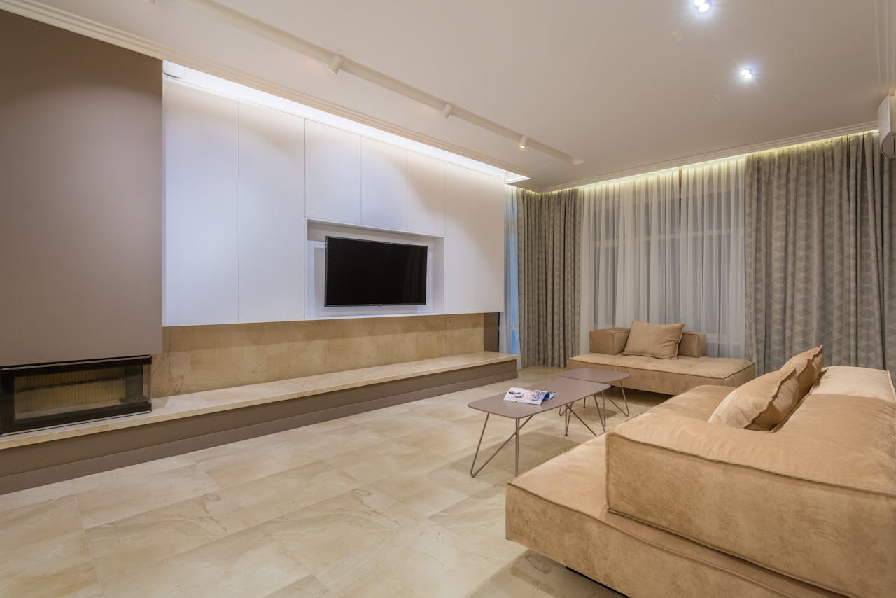 Minimalist design of spacious living room with big comfortable beige sofas placed in front of TV in modern apartment with illuminated stretch ceiling