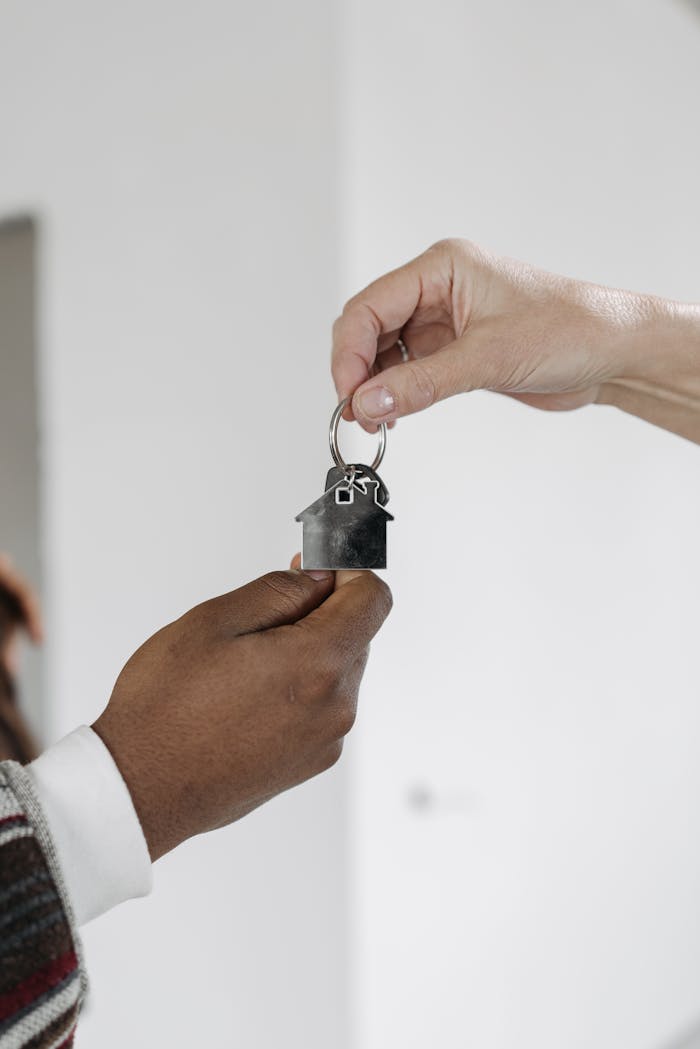 A close-up of two hands exchanging a house-shaped key, symbolizing a home purchase or rental agreement.
